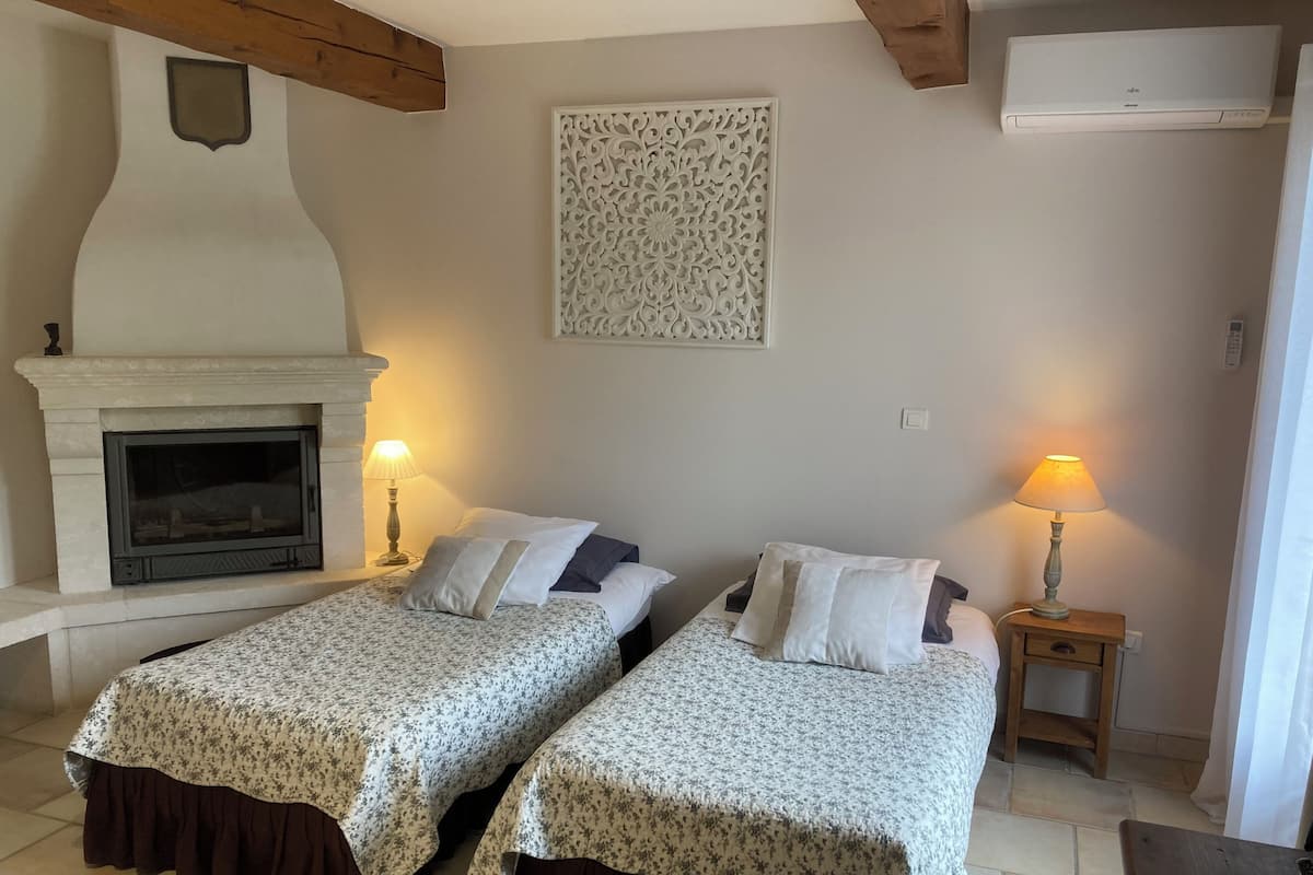 Una habitación con dos camas, chimenea, aire acondicionado instalado en la pared y un panel decorativo.