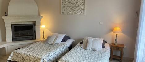 Une chambre avec deux lits, une cheminée, un climatiseur mural et un panneau décoratif.
