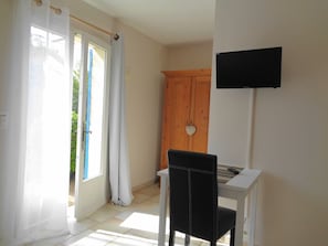 A room with a white desk, a black chair, a wooden wardrobe, and a TV mounted on the wall. - Le clos des lavandes (Lacoste (Provence))