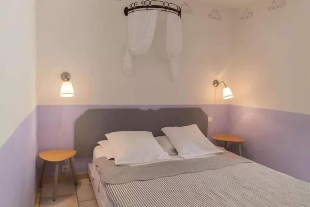A bedroom with a bed, two bedside tables, a nightstand, a wall-mounted lamp, and a ceiling-mounted canopy.