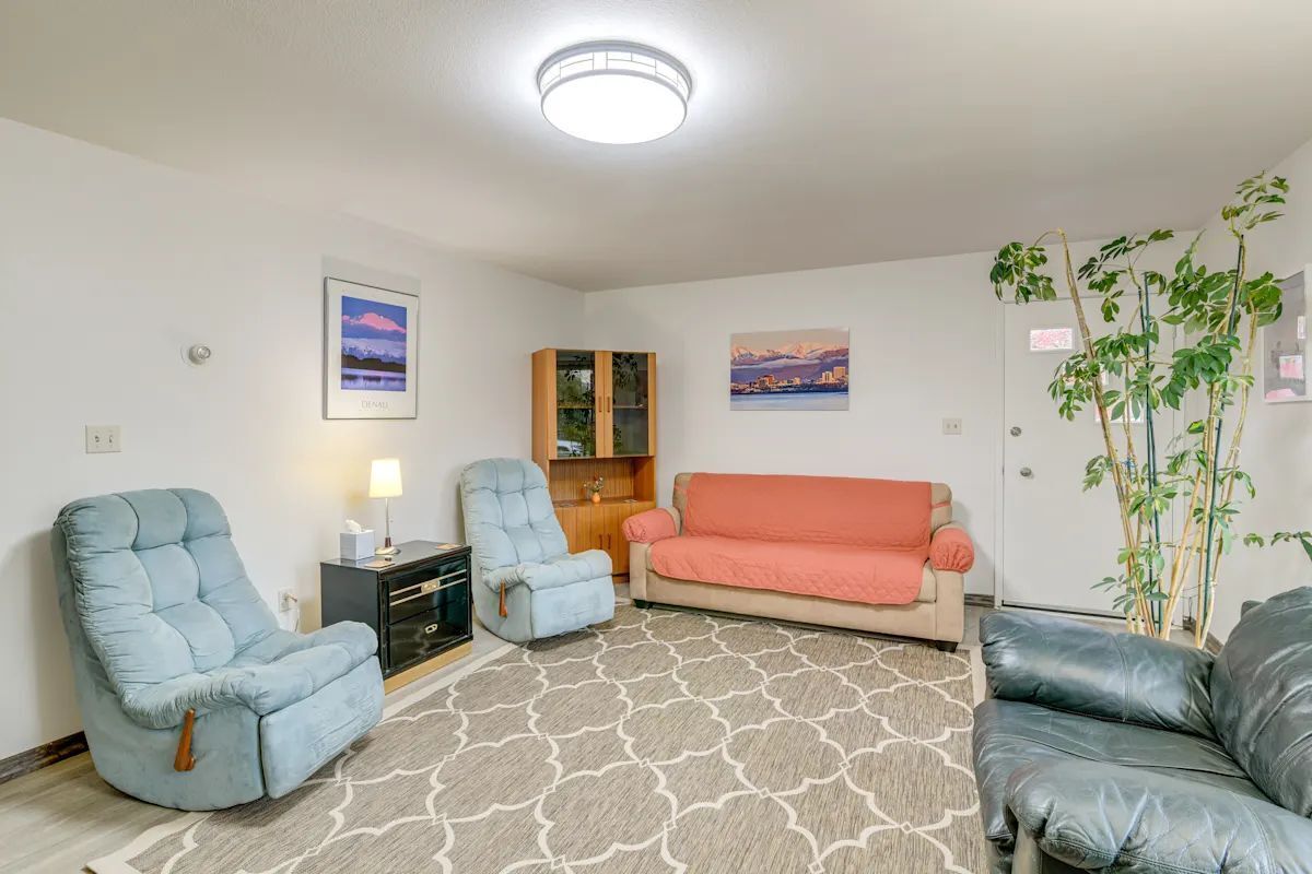 A living room with a sofa, two armchairs, a rug, a cabinet, and a plant.