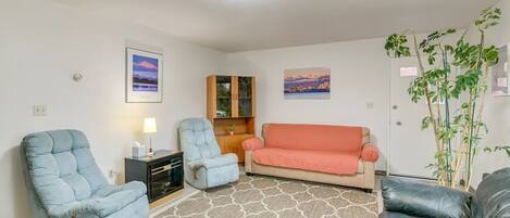 A living room with a sofa, two armchairs, a rug, a cabinet, and a plant.