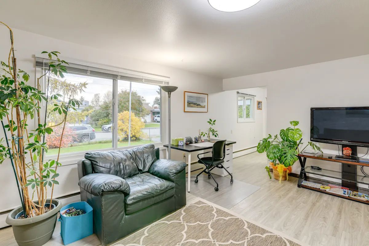 A modern living room with a leather sofa, a desk, a television, and potted plants.