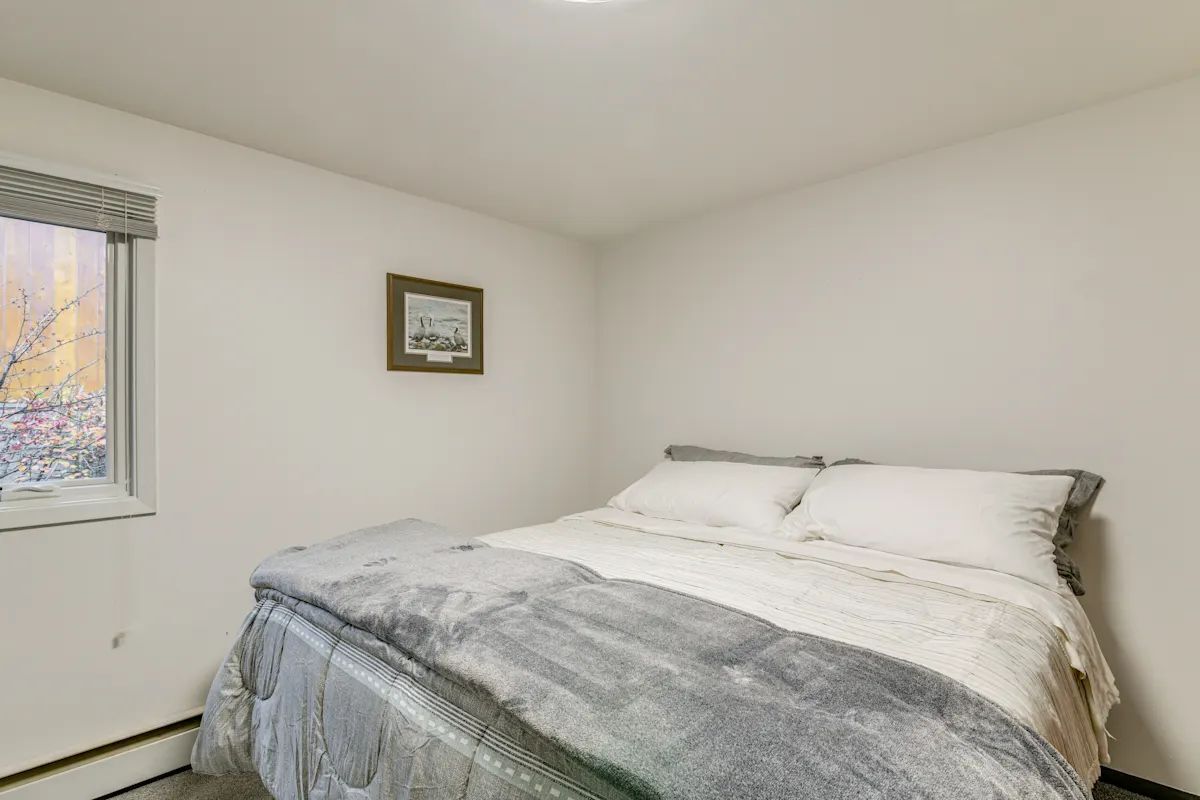 A bedroom with a bed, a window with blinds, and a framed picture on the wall.