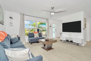Ein modernes Wohnzimmer mit Sofa, Couchtisch, Fernseher und großen Fenstern.