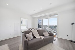Ein modernes Wohnzimmer mit grauem Sofa, einem Esstisch und Blick auf die Stadt durch große Fenster.
