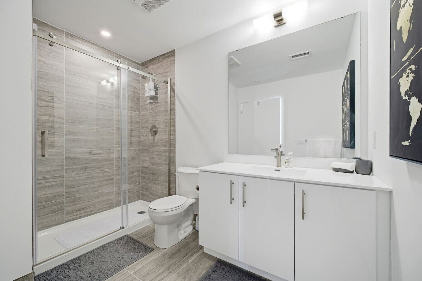 Een moderne badkamer met een douche met glazen wand, een toilet, een wit wastafelmeubel met spiegel, en een handdoek op het aanrecht.