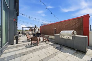Een terras buiten met een barbecue, zithoek en lichtjes.