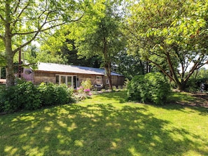 A rustic house with a metal roof, surrounded by lush greenery and a well-maintained lawn. - Woodman's Lodge (Moelfre)
