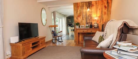 A living room with a television, wooden furniture, a rocking chair, and a dining area with a wooden wall.
