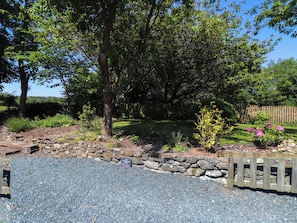 A garden with a stone wall, a wooden fence, and various plants. - Woodman's Lodge (Moelfre)