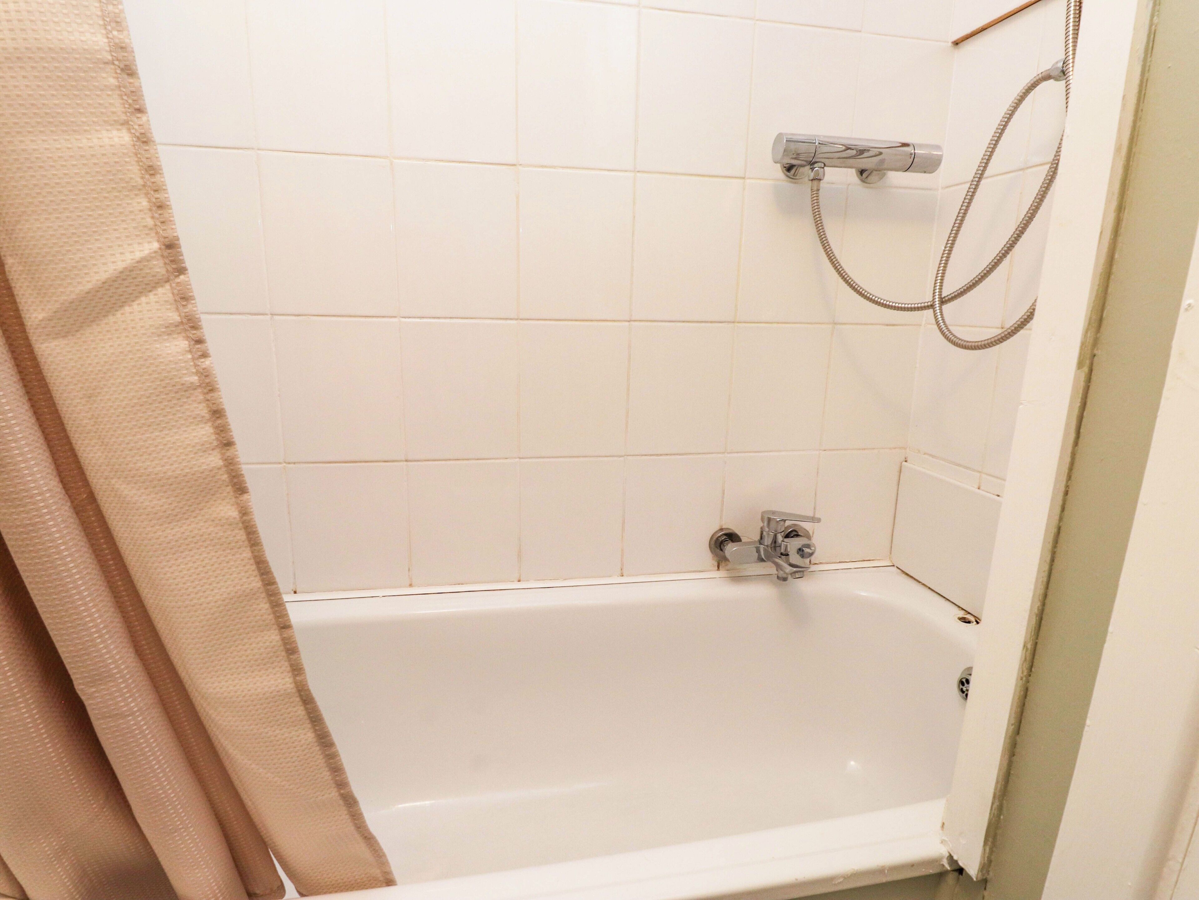 Un baño con paredes de azulejos blancos, una bañera y una ducha con manguera.