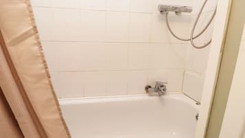 Un baño con paredes de azulejos blancos, una bañera y una ducha con manguera.