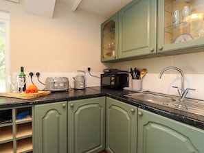 A kitchen with green cabinets, a toaster, a kettle, and a sink. - Woodman's Lodge (Moelfre)