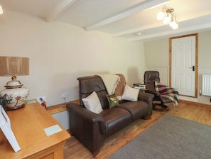 A living room with a brown leather sofa, a wooden coffee table, a lamp, and a mirror on the wall. - Woodman's Lodge (Moelfre)