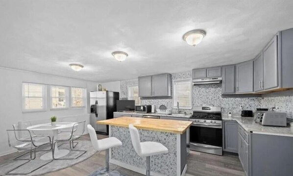 Una cocina moderna con una isla central, electrodomésticos de acero inoxidable y una zona de comedor con una mesa redonda y sillas.