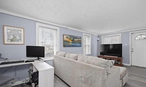 A living room with a sofa, a TV, a computer desk, and artwork on the walls.