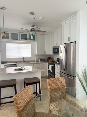 Una cocina moderna con armarios blancos, electrodomésticos de acero inoxidable, una isla central con taburetes y un ventilador de techo.