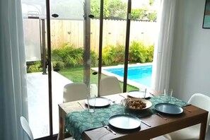 Ein Esstisch mit Tellern, Gläsern und einer Schüssel, vor einer Kulisse aus Holzzaun und Schwimmbecken.