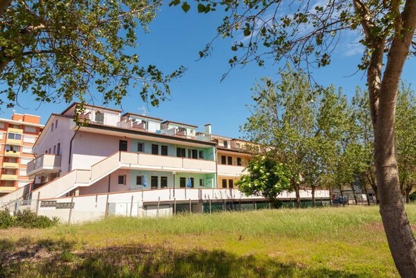 Un immeuble résidentiel à plusieurs étages, doté de balcons, entouré d’arbres et d’une zone verdoyante.