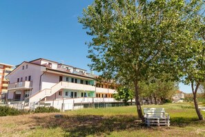 A multi-story building with balconies, a grassy area, and a bench. - Arcobaleno Residence, Paguro Two-Room Apartment for 4 People (Chioggia)