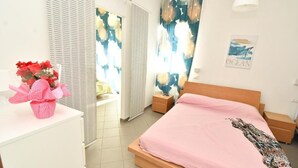 Une chambre à coucher comprenant un lit, une table de chevet, une commode, une fenêtre avec des rideaux et une œuvre d’art murale.