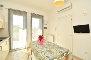 A room with a bed, a table with a patterned tablecloth, a TV on the wall, and a window with curtains. - Residenz Arcobaleno, Stella Marina 1 Two-Room Apartment for 4 People (Chioggia)