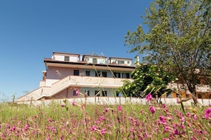 A multi-story building with a balcony, surrounded by a field of pink flowers. - Residenz Arcobaleno, Stella Marina 1 Two-Room Apartment for 4 People (Chioggia)