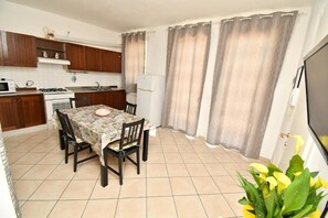A compact kitchen with a dining area, a stove, a refrigerator, and a TV. - Residenz Arcobaleno, "Ostrica" Two-Room Apartment for 4 People (Chioggia)