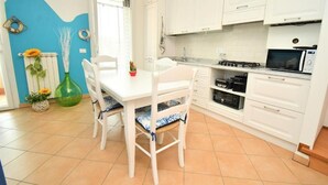 Una cocina con alacenas blancas, una mesa de comedor con sillas, un microondas y una estufa a gas.