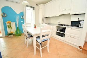 A kitchen with white cabinets, a dining table with chairs, a microwave, and a gas stove. - Residenz Arcobaleno, "Granchio" Three-Room Apartment for 6 People (Chioggia)