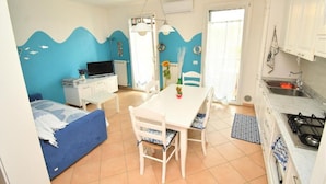 Una habitación funcional con cama, mesa de comedor con sillas, kitchenette y baño.