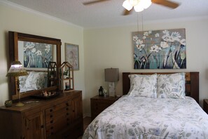 Een slaapkamer met een bed, dressoir, nachtkastje, lamp en kunstwerken aan de wand.