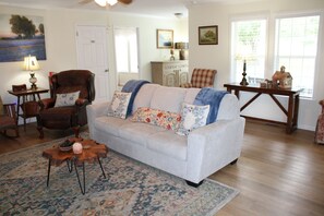 Een woonkamer met een bank, fauteuils, een houten bijzettafeltje en een vloerkleed met een patroon.