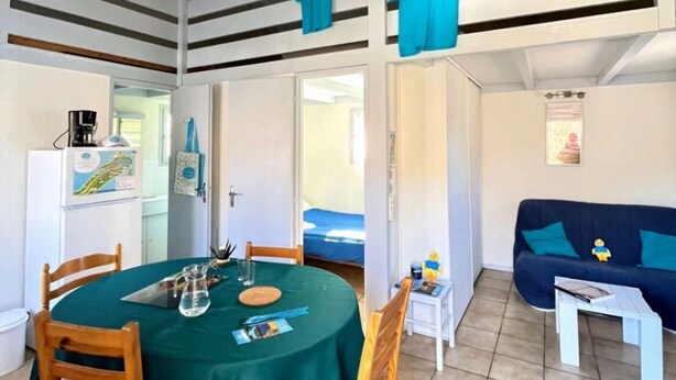 A compact living space with a dining area, a sofa, and a small table. - Chalet 3 étoiles - Piscine  - eeccga (Arnac)