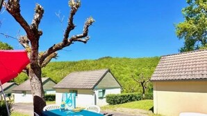A patio with a table and chairs, a red umbrella, and a tree. - Chalet 3 étoiles - Piscine  - eeccga (Arnac)
