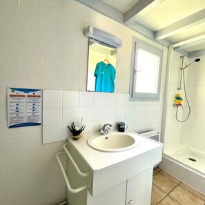 Ein Badezimmer mit einem weißen Waschbecken, einem Spiegel, einem Handtuchhalter und einer Dusche.