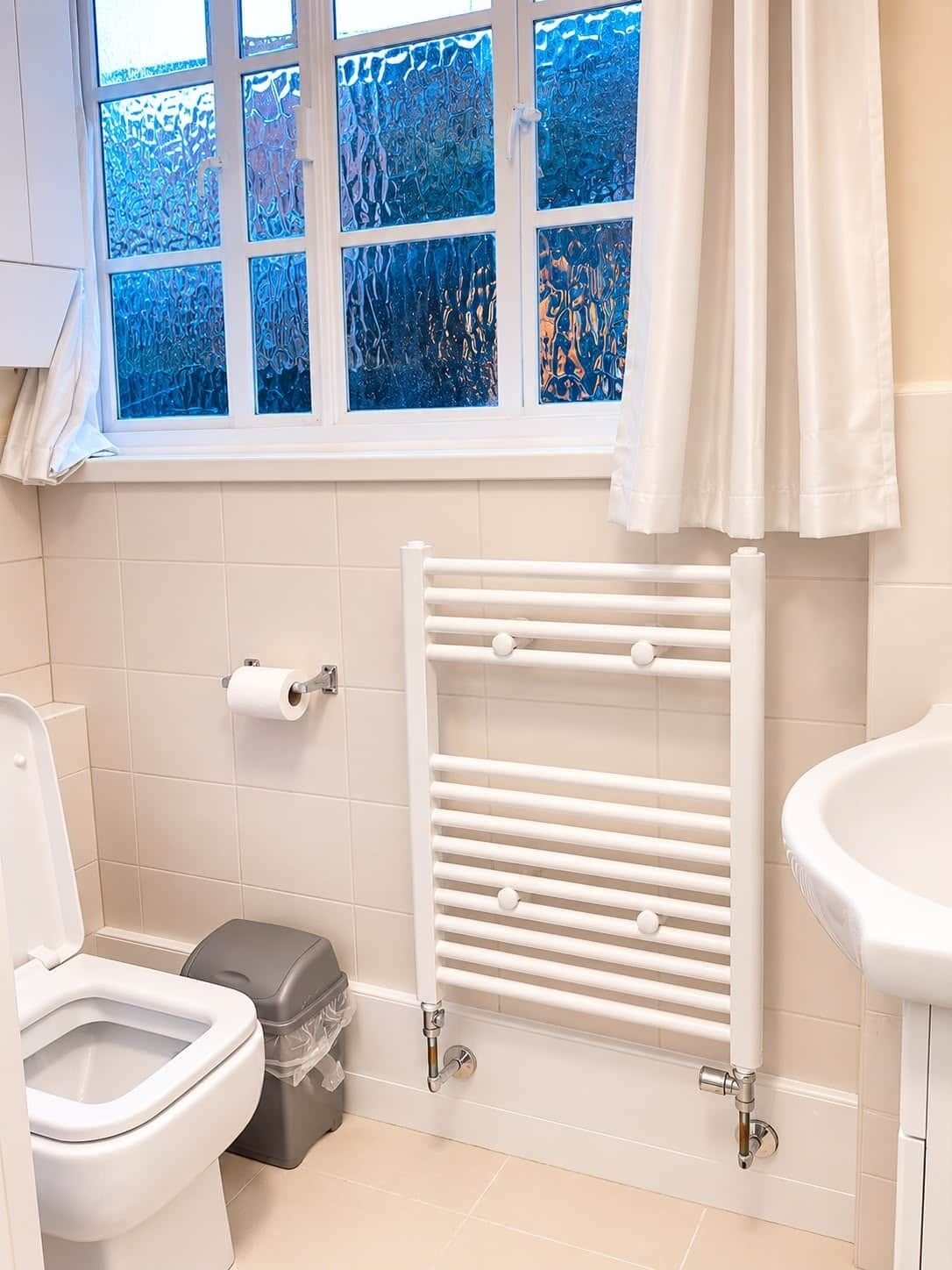 A bathroom with a toilet, bidet, white radiator, and a window with frosted glass.