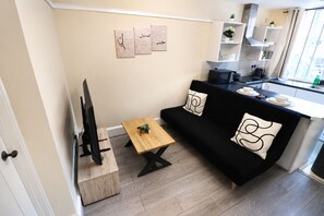 A compact living space with a sofa, a coffee table, a television on a wooden stand, and a kitchen area with a countertop and cabinets. - Apartment Opp Leicester Train Station | Central (Leicester)