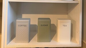 Un mueble blanco con estantes y recipientes etiquetados para café, azúcar y té.