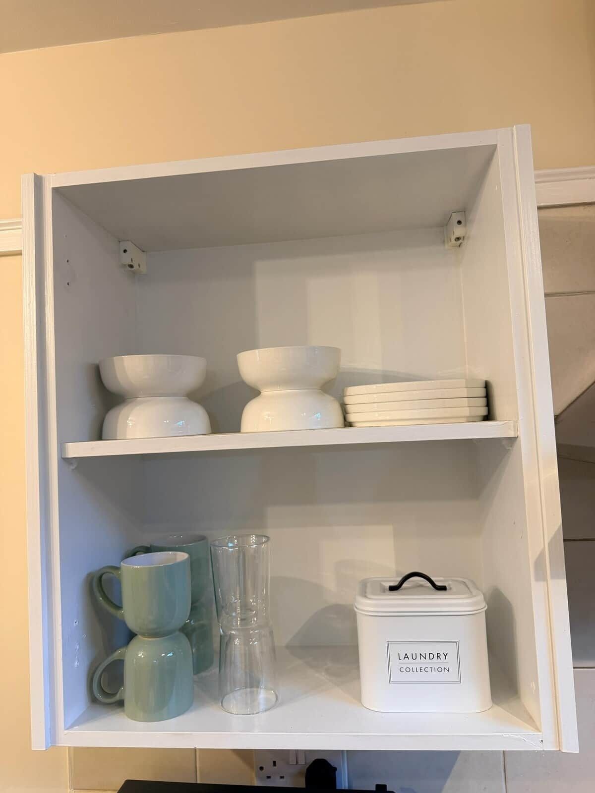 A white storage unit with shelves containing bowls, plates, and a container labeled 'laundry collection'.
