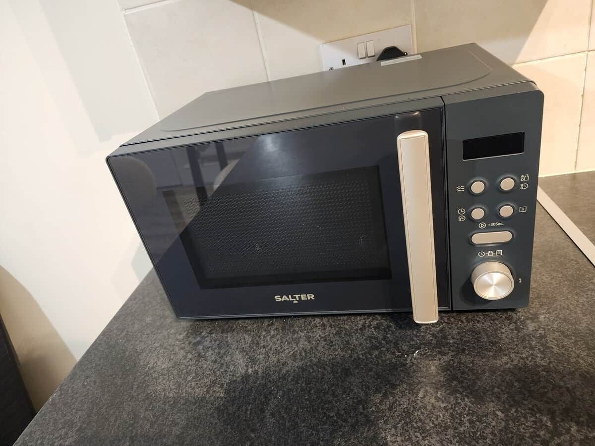A black microwave oven with a digital display and control buttons on a kitchen counter.