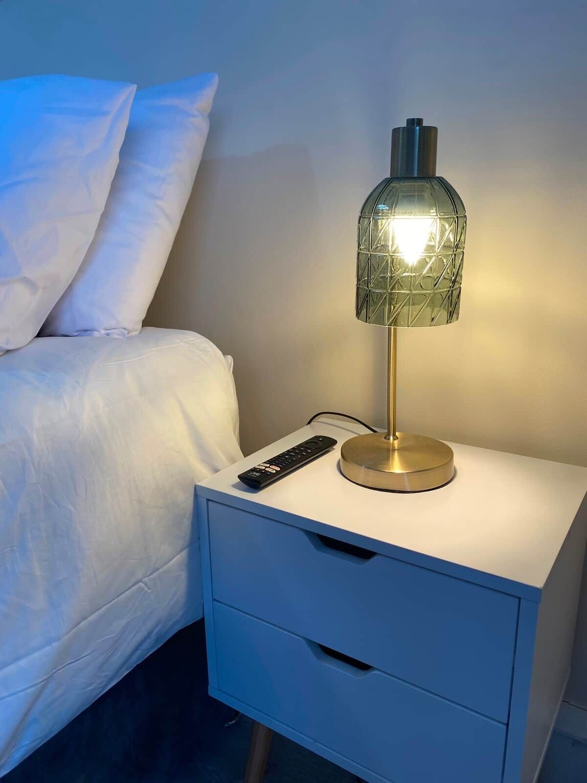 A bed with white bedding, a bedside table with a lamp, and a remote control.