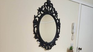 Una habitación con un radiador blanco, un espejo negro ornamentado y dos pequeñas macetas con plantas sobre una estantería.