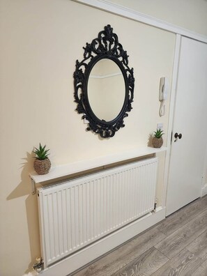 A room with a white radiator, a black ornate mirror, and two small potted plants on a shelf. - Apartment Opp Leicester Train Station | Central (Leicester)