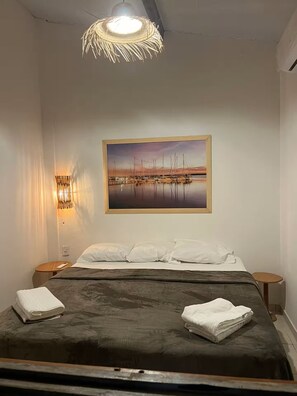 Habitació d'hotel amb un llit, un quadre d'un port esportiu, una làmpada de paret i un lluminari al sostre.