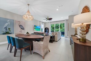 Ein moderner Essbereich mit einem runden Tisch, Stühlen, einer Pendelleuchte und einem Fernseher im Hintergrund.