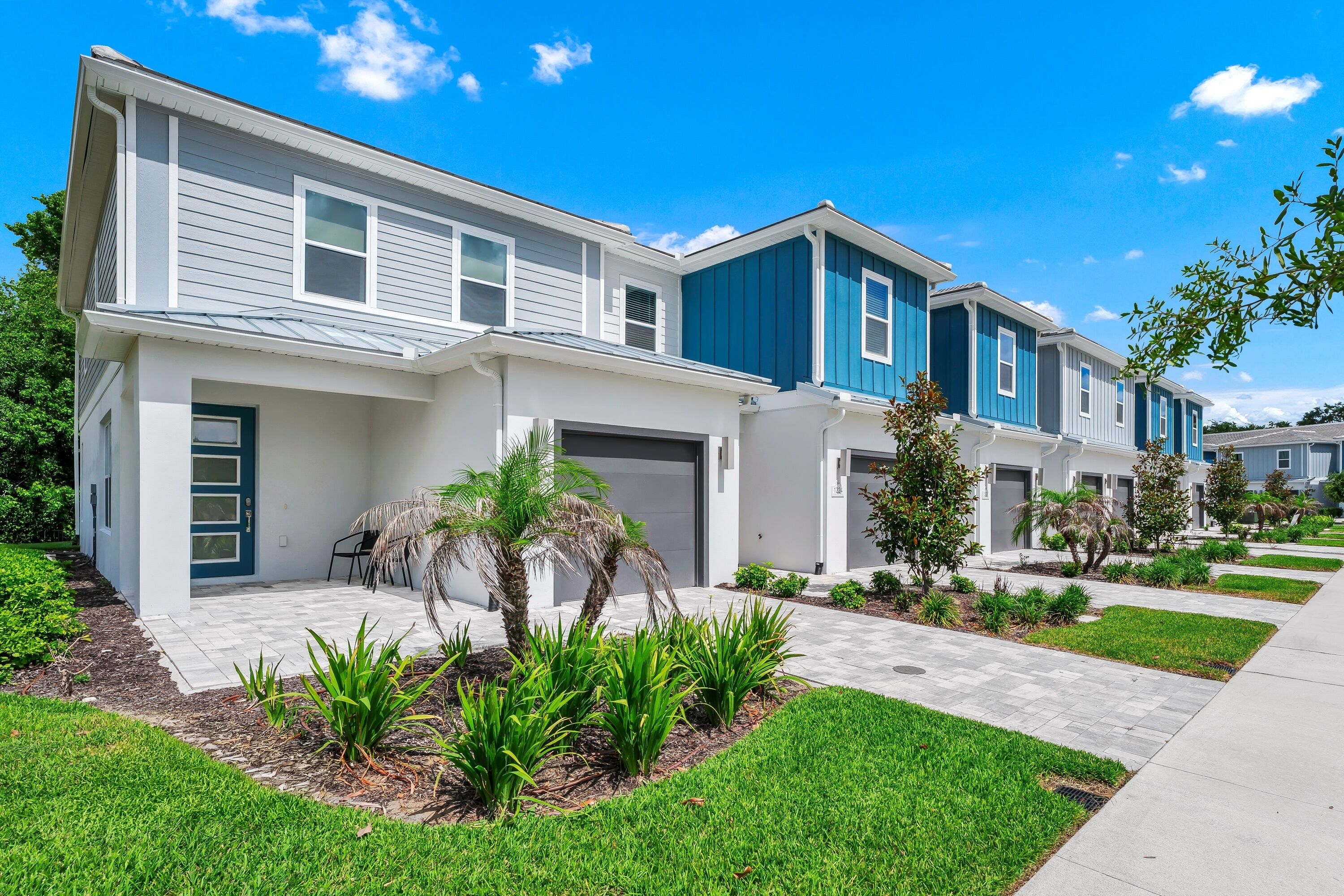 A row of modern two-story townhouses with attached garages, a well-maintained lawn, and a clear sky.