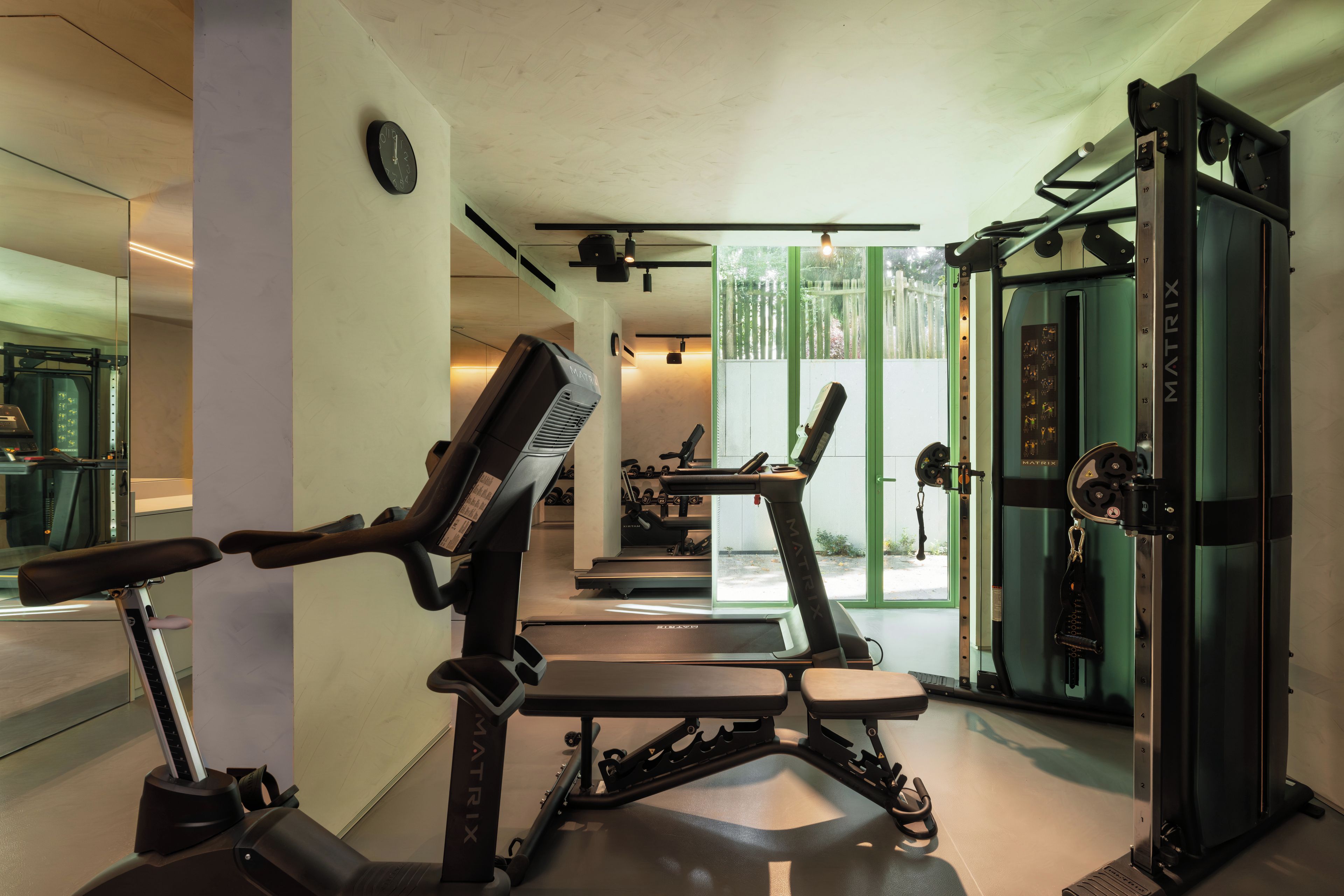 Un gimnasio con equipo de ejercicio, un espejo grande y un ventanal con vistas a árboles.
