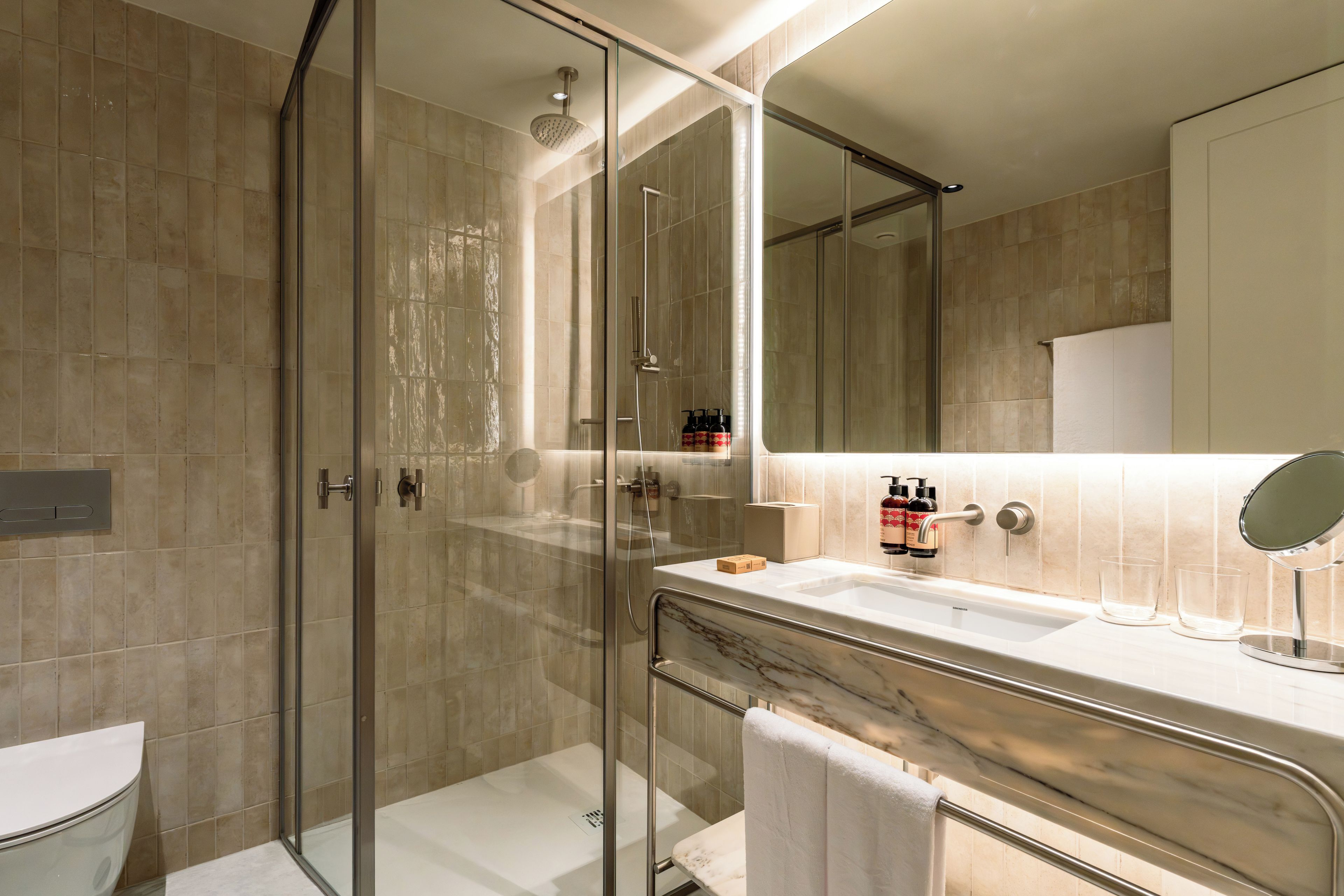 A modern bathroom with a glass-enclosed shower, a marble vanity, and a large mirror.